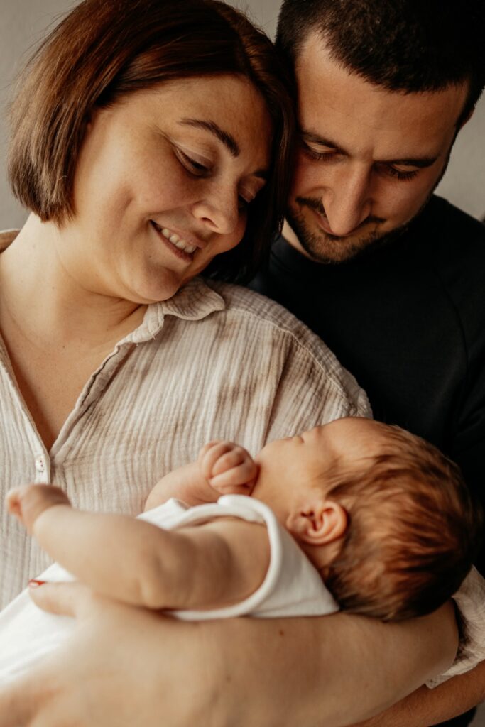 Mama und Papa halten ihre Köpfe nah aneinander und schauen glücklich auf ihr Baby runter.