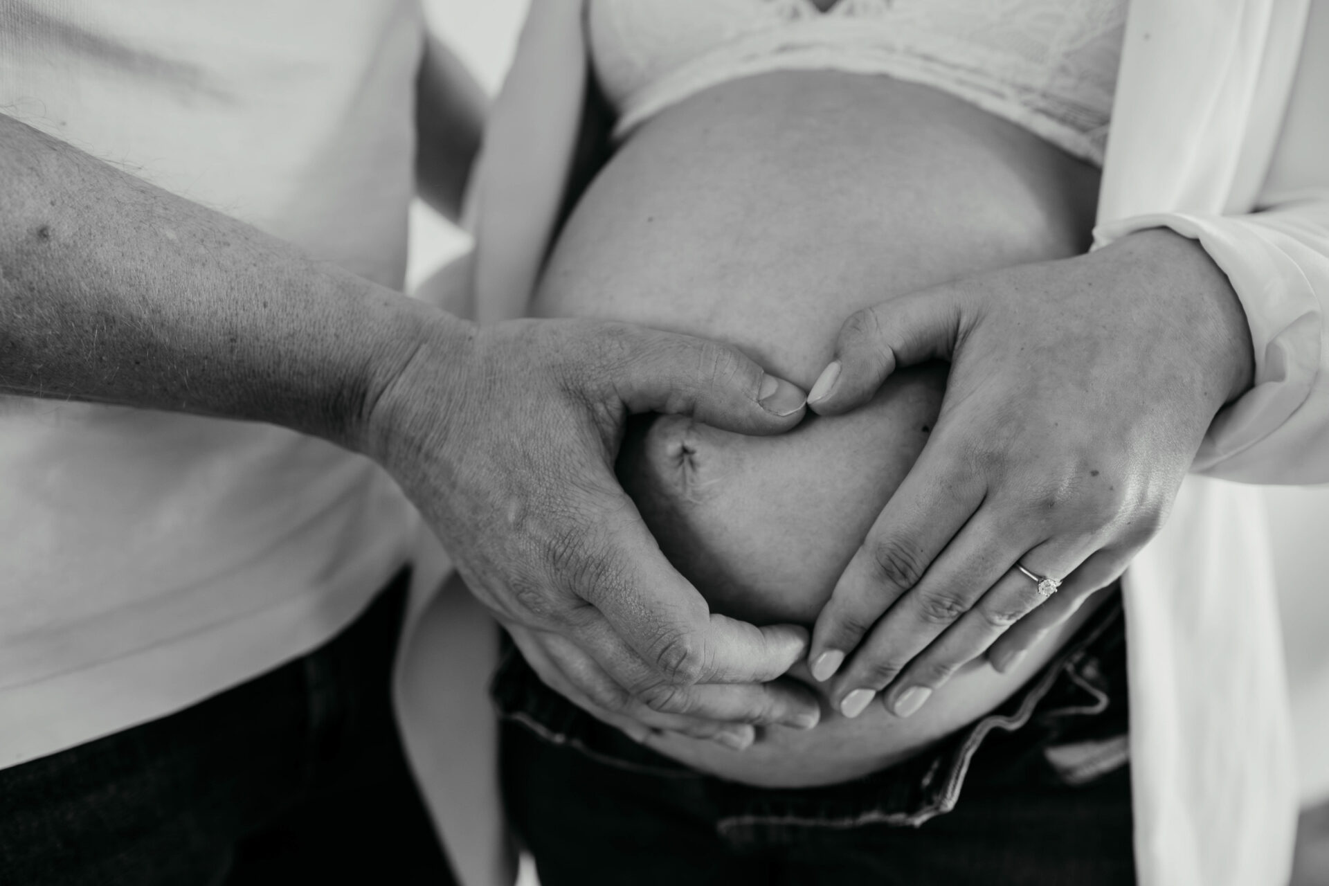 Schwarz-weiß Bild auf dem der Mann und die Frau mit den Händen ein Herz vor dem Bauch formen.