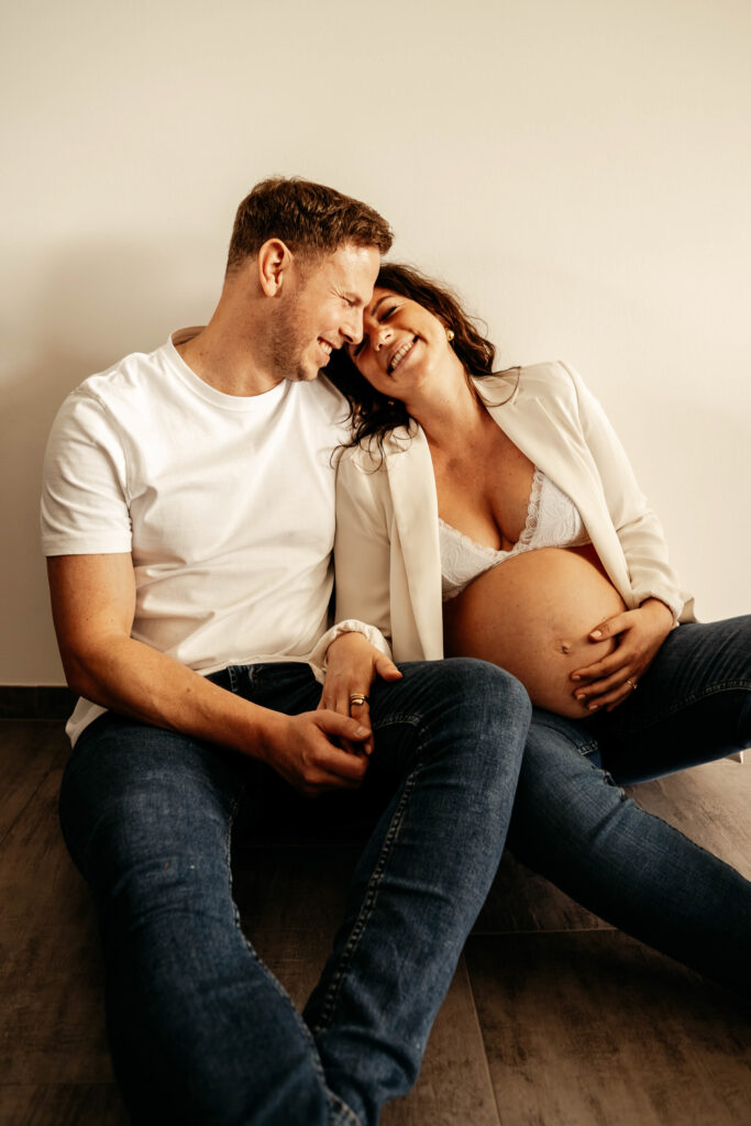 Pärchen bei einem Babybauchshooting sitzen aneinander gekuschelt auf dem Boden