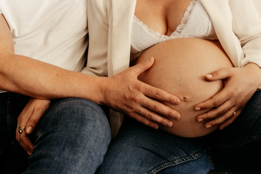 in Bild von einem nackten Babybauch auf dem Mann und Frau ire Hand gelegt haben.