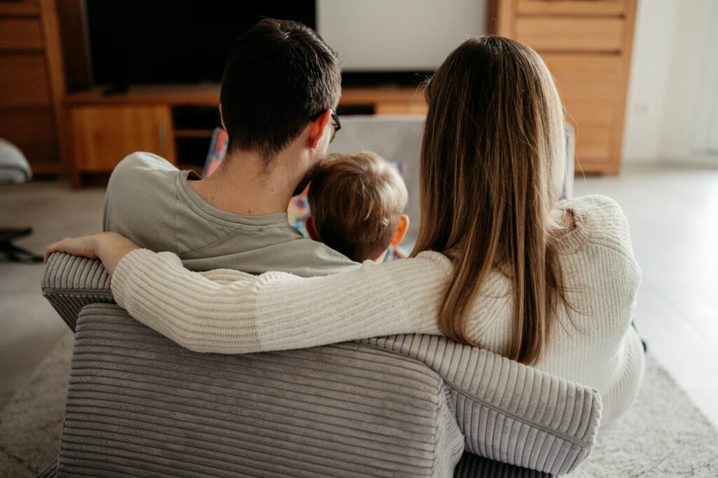 Das Foto zeigt die Hinterköpfe der Familie. Die Mama legt den Arm um den Papa, das Kind sitzt zwischen den beiden.