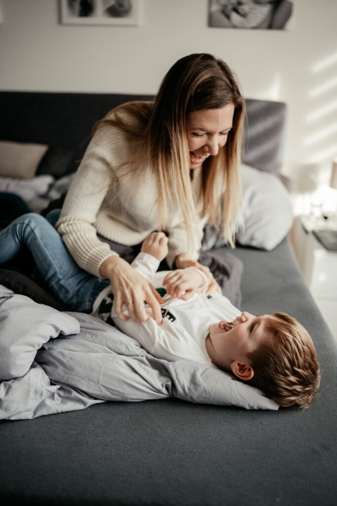 Mama kitzelt Sohn auf dem Bett, beide lachen herzhaft.