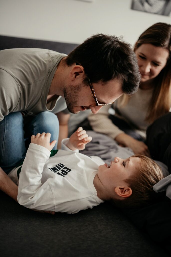 Vater kitzelt den Sohn auf dem Bett, beide lachen.