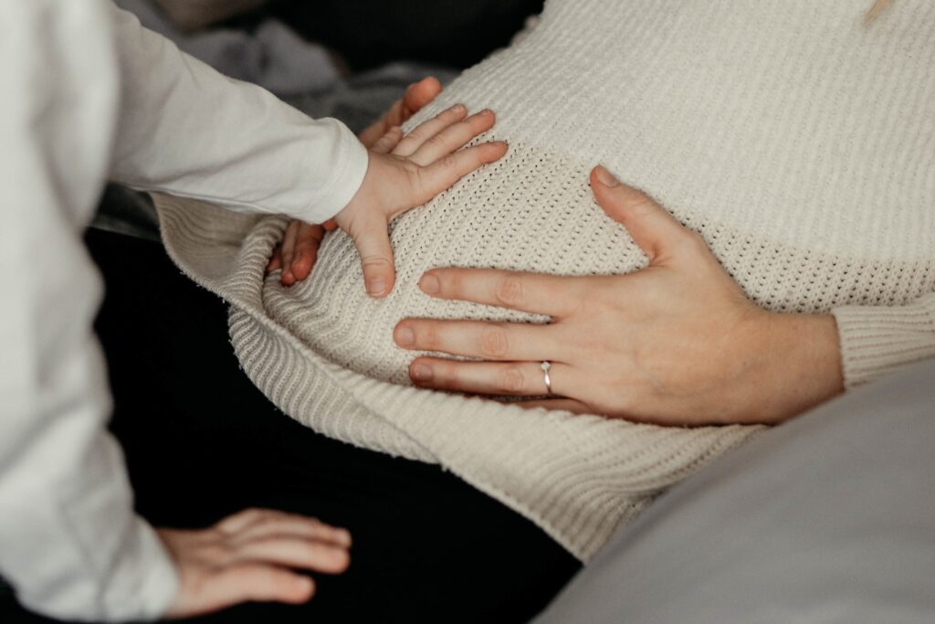 Nachaufnahme vom kleinen Babybauch der Mama. Der Sohn hält seine Hand auf dem Bauch.