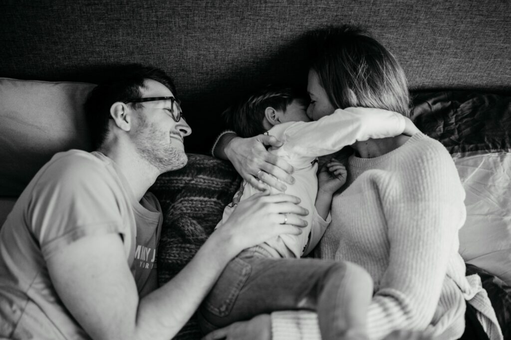 Familie kuschelt gemeinsam im Bett. Sohn umarmt die Mama