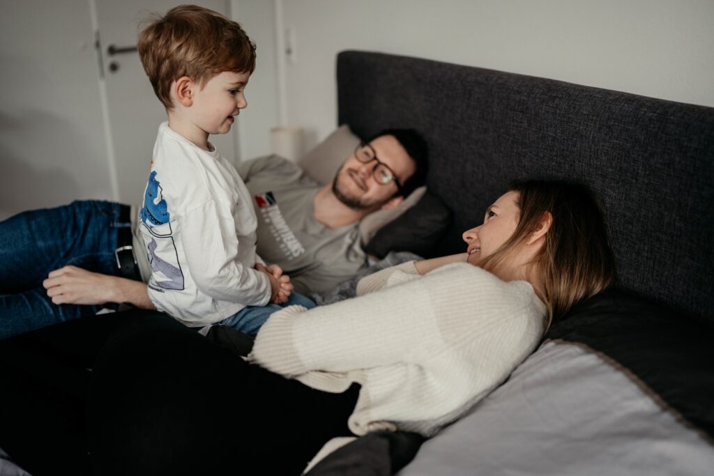 Eltern liegen auf dem Bett, der dreijährige Sohn kniet zwischen den beiden.