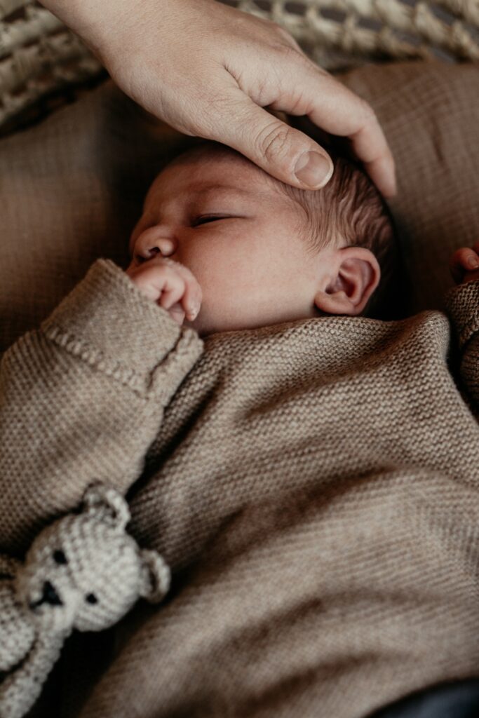 Foto von einem Neugeborenen-Homeshooting. Das Bild zeigt das Baby wie es auf dem Rücken liegt. Die Mama hält ihre Hand auf dem Kopf des Babys